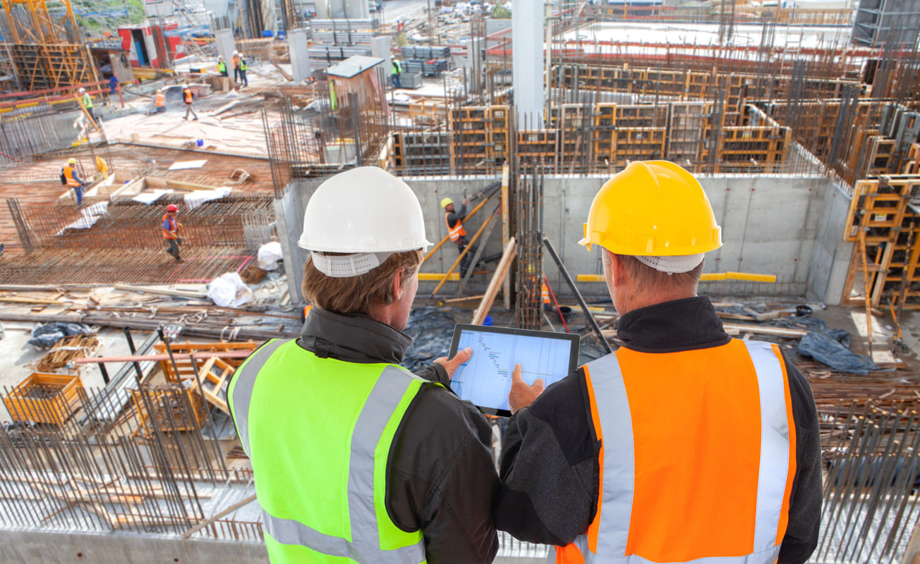 Un trabajador de la construcción discutiendo los planes de construcción con un arquitecto que sostiene una tableta.